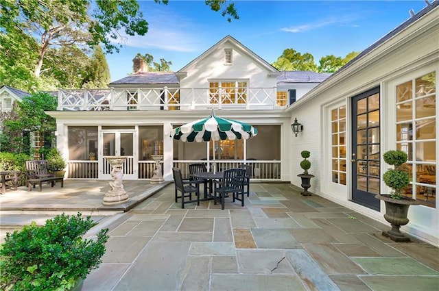 rear view of house with a balcony, a patio area, a chimney, french doors, and outdoor dining area