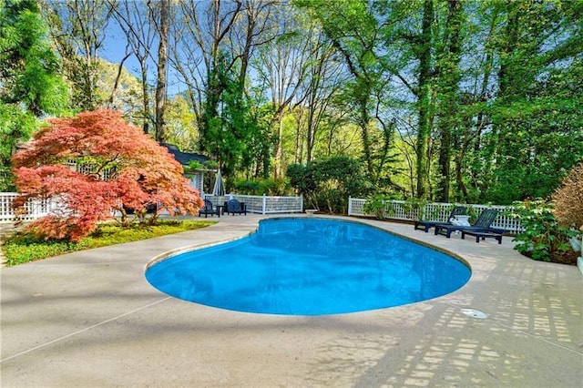 view of pool with a patio, fence, and view of wooded area