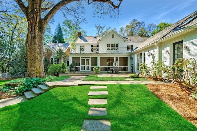 rear view of house featuring a balcony, a chimney, french doors, and a lawn