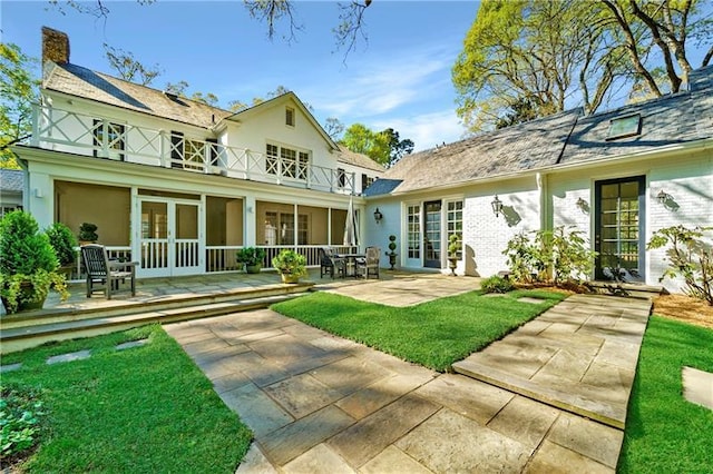 rear view of property featuring a balcony, a chimney, french doors, a patio area, and a yard