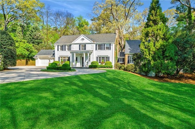 colonial-style house featuring concrete driveway, a front yard, an attached garage, and covered porch