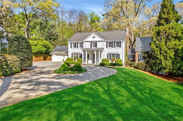colonial inspired home featuring curved driveway, a front lawn, an attached garage, and covered porch