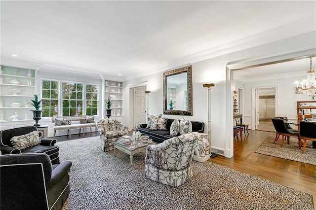 living room featuring ornamental molding, a chandelier, wood finished floors, and built in features