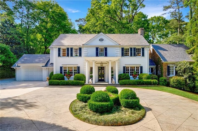 colonial-style house featuring curved driveway, a chimney, a garage, and stucco siding