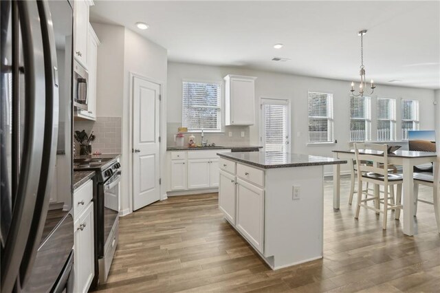 kitchen with decorative light fixtures, white cabinetry, stainless steel appliances, backsplash, and a chandelier