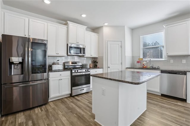 kitchen with a sink, appliances with stainless steel finishes, wood finished floors, and white cabinetry