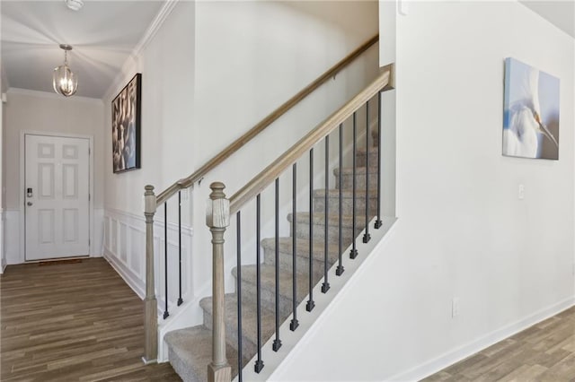 stairway with a notable chandelier, wood finished floors, a decorative wall, wainscoting, and crown molding