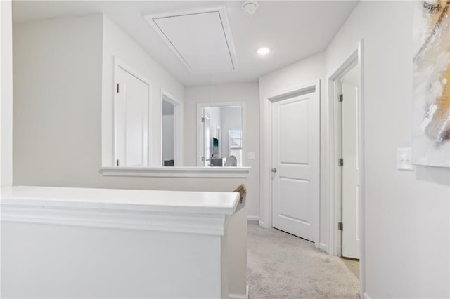hallway featuring baseboards, light colored carpet, and attic access