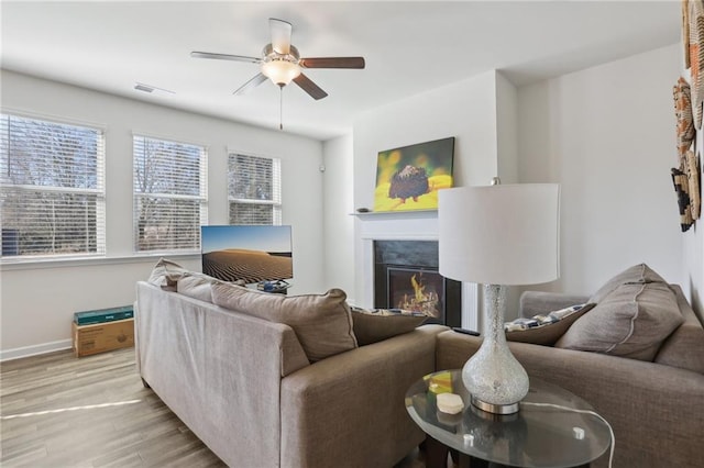 living area featuring visible vents, a ceiling fan, wood finished floors, a fireplace, and baseboards