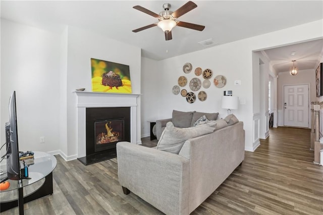 living area with a glass covered fireplace, wood finished floors, visible vents, and ceiling fan
