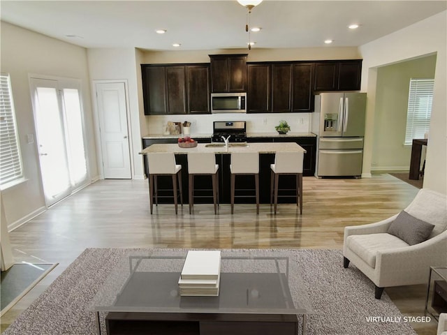 kitchen featuring dark brown cabinetry, appliances with stainless steel finishes, a breakfast bar, and a kitchen island with sink