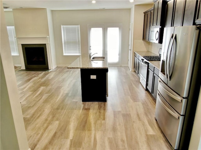 kitchen with an island with sink, light hardwood / wood-style flooring, stainless steel appliances, and light stone counters