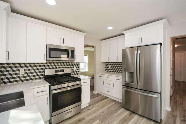 kitchen with light hardwood / wood-style flooring, backsplash, white cabinets, and stainless steel appliances