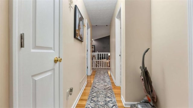 hall featuring visible vents, a textured ceiling, light wood finished floors, and baseboards