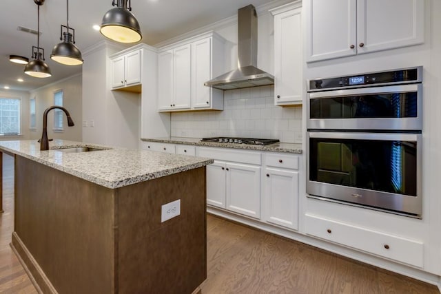 kitchen with sink, hanging light fixtures, stainless steel appliances, light stone countertops, and wall chimney exhaust hood