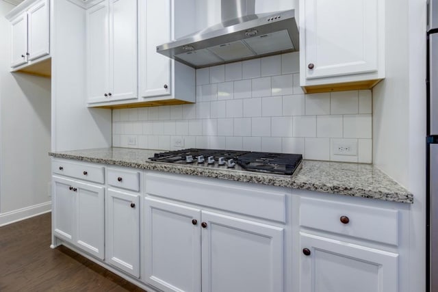 kitchen with wall chimney range hood, white cabinetry, light stone countertops, stainless steel gas cooktop, and decorative backsplash