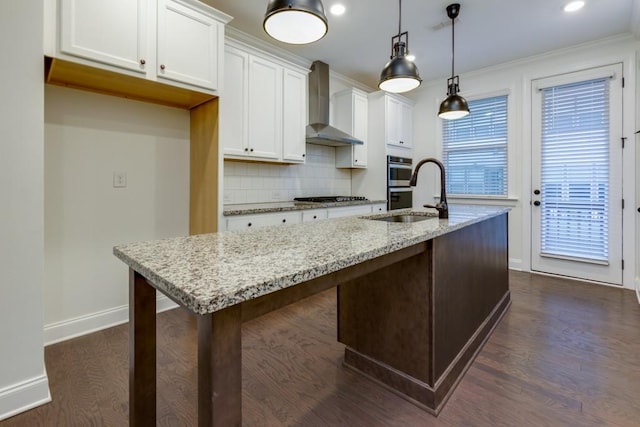 kitchen featuring white cabinetry, hanging light fixtures, light stone countertops, a center island with sink, and wall chimney exhaust hood