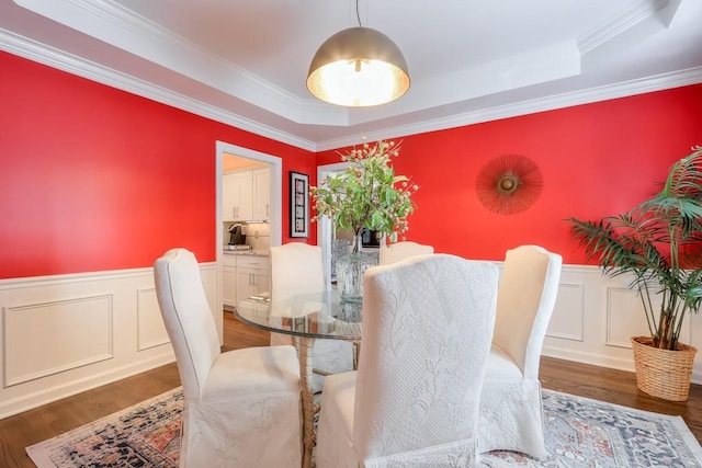 dining area with a tray ceiling, wainscoting, and wood finished floors