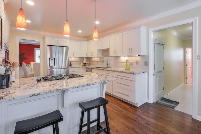 kitchen featuring a peninsula, a sink, white cabinetry, appliances with stainless steel finishes, and crown molding