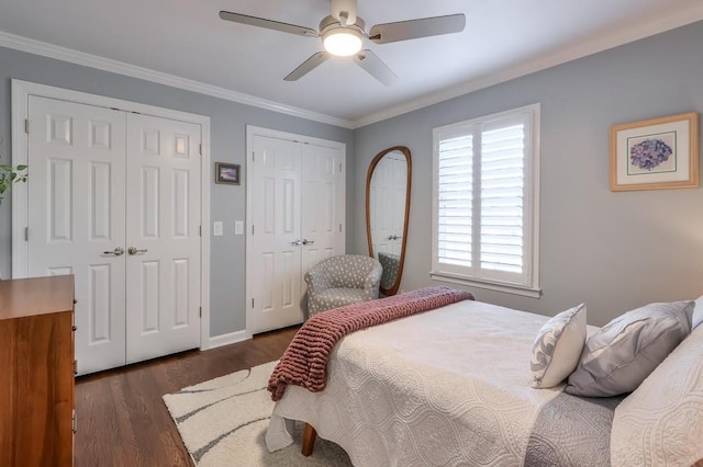 bedroom with dark wood-style flooring, two closets, ornamental molding, ceiling fan, and baseboards