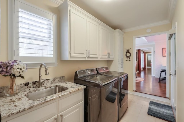 clothes washing area featuring cabinet space, light tile patterned floors, washing machine and clothes dryer, crown molding, and a sink