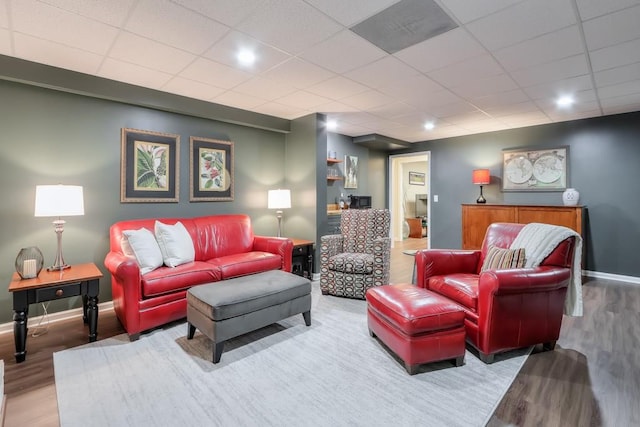 living area with a drop ceiling, baseboards, and wood finished floors