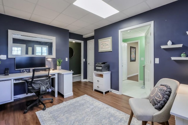 home office featuring baseboards, a drop ceiling, and wood finished floors