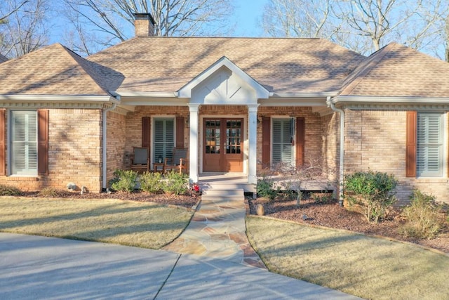 ranch-style house with roof with shingles, a chimney, french doors, and brick siding