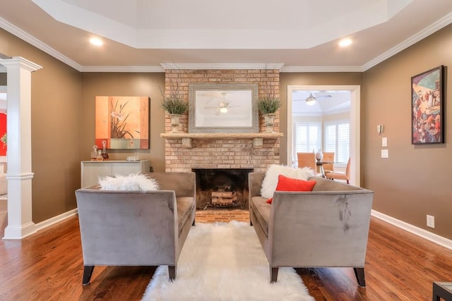 living area featuring a brick fireplace, decorative columns, baseboards, and wood finished floors