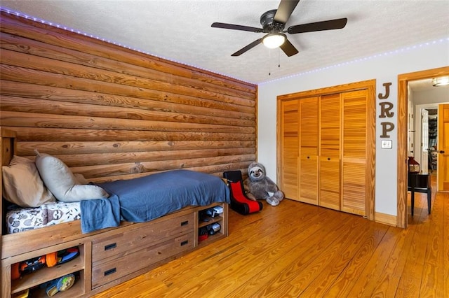 bedroom featuring a textured ceiling, ceiling fan, log walls, light hardwood / wood-style floors, and a closet