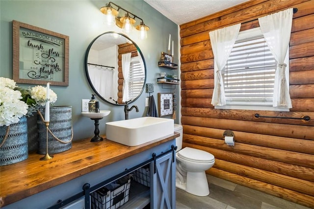 bathroom with log walls, a textured ceiling, toilet, vanity, and hardwood / wood-style flooring