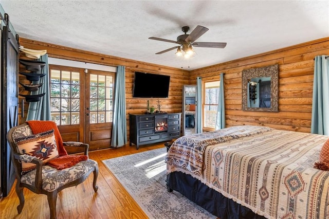 bedroom featuring french doors, ceiling fan, a textured ceiling, rustic walls, and wood-type flooring