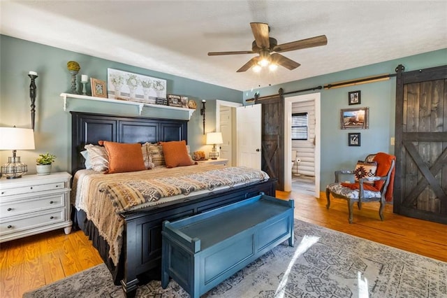 bedroom with ceiling fan, a barn door, light hardwood / wood-style floors, and connected bathroom