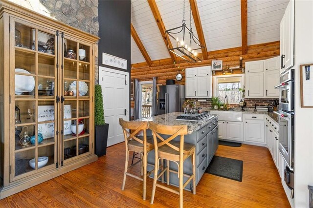 kitchen with a center island, high vaulted ceiling, stainless steel refrigerator with ice dispenser, rustic walls, and white cabinetry