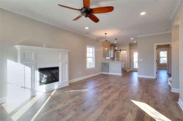 unfurnished living room with wood-type flooring, a barn door, ornamental molding, and ceiling fan