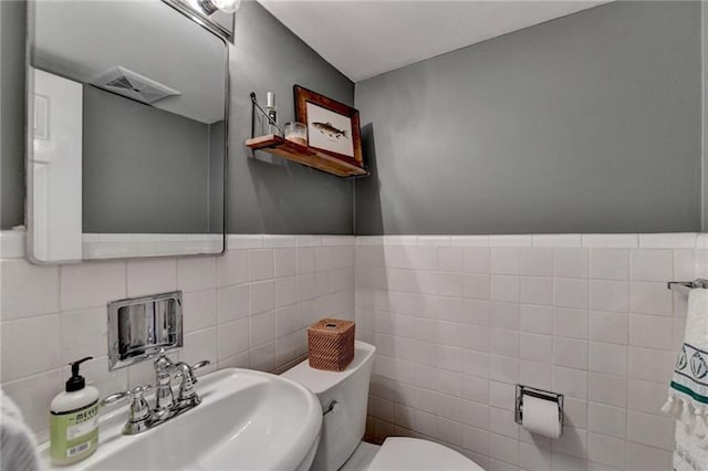 half bath featuring visible vents, toilet, tile walls, and a sink