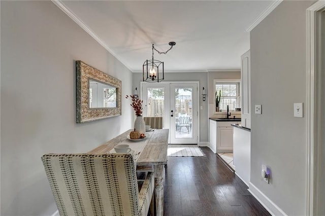 unfurnished dining area with a sink, dark wood-style floors, crown molding, baseboards, and a chandelier