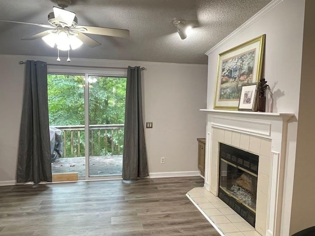 unfurnished living room with wood-type flooring, a textured ceiling, a tile fireplace, ceiling fan, and ornamental molding