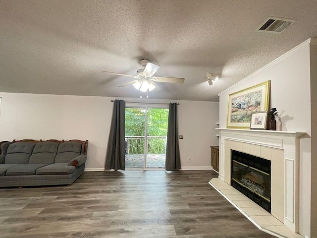 living room with hardwood / wood-style flooring, ornamental molding, a textured ceiling, a fireplace, and ceiling fan