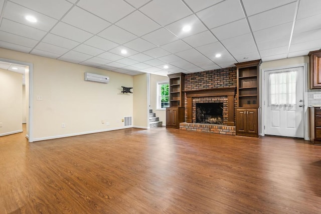 unfurnished living room with a wall unit AC, plenty of natural light, dark wood-type flooring, and a brick fireplace