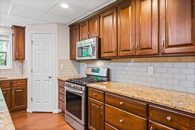 kitchen with a paneled ceiling, light stone counters, stainless steel appliances, and light hardwood / wood-style flooring