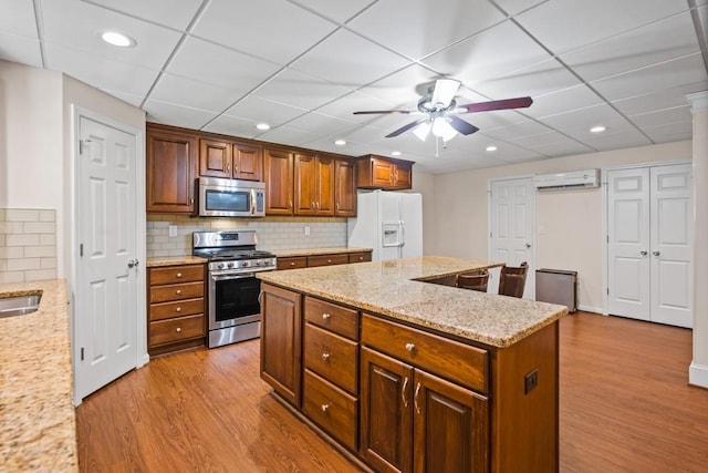 kitchen with a wall mounted air conditioner, appliances with stainless steel finishes, light hardwood / wood-style floors, and a kitchen island