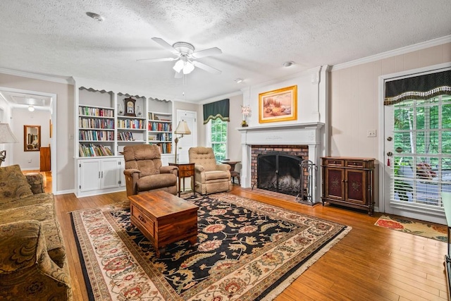 living room with a brick fireplace, light hardwood / wood-style flooring, ceiling fan, ornamental molding, and a textured ceiling