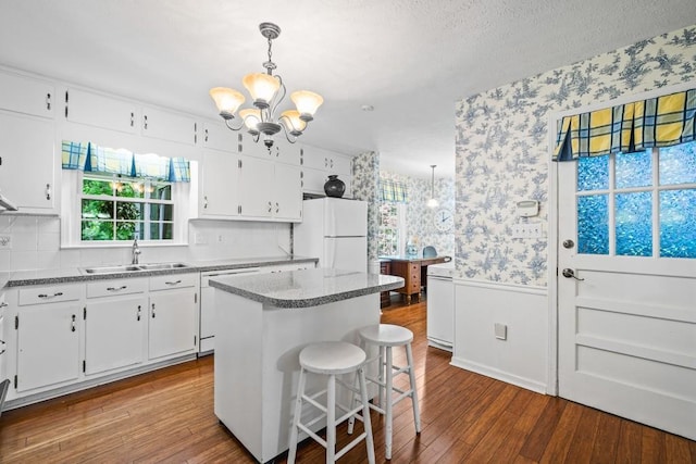 kitchen featuring sink, a kitchen island, pendant lighting, white appliances, and white cabinets