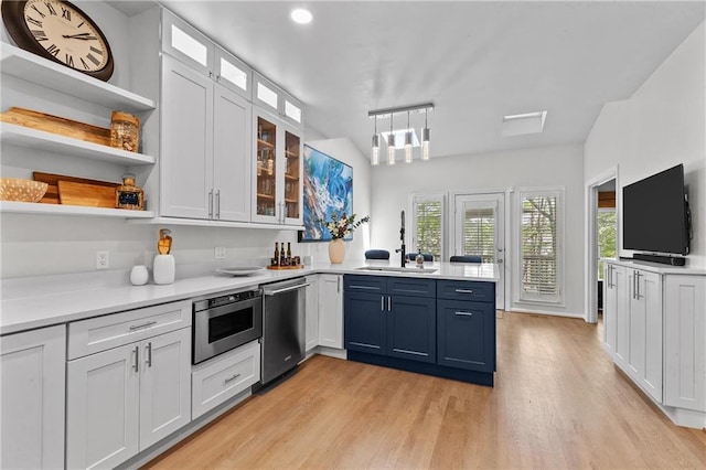 kitchen featuring open shelves, a sink, dishwasher, light wood-style flooring, and a peninsula