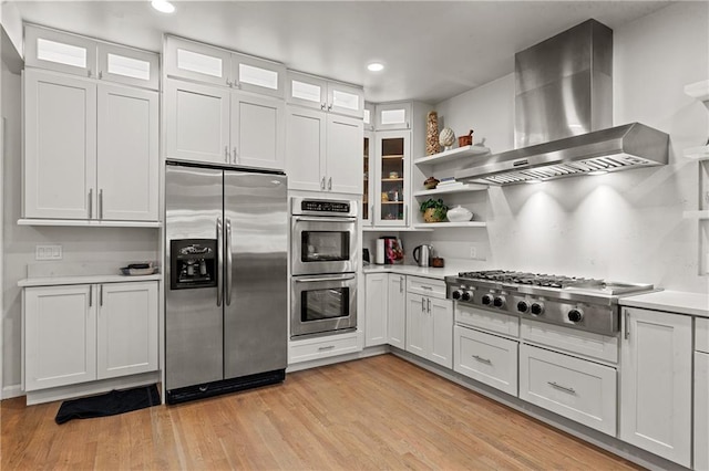 kitchen with open shelves, light countertops, white cabinets, wall chimney exhaust hood, and appliances with stainless steel finishes