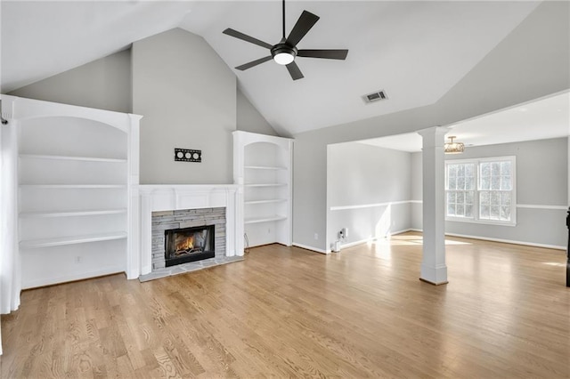 unfurnished living room featuring visible vents, ceiling fan, wood finished floors, a lit fireplace, and ornate columns