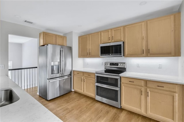 kitchen featuring visible vents, appliances with stainless steel finishes, light brown cabinetry, light wood finished floors, and tasteful backsplash