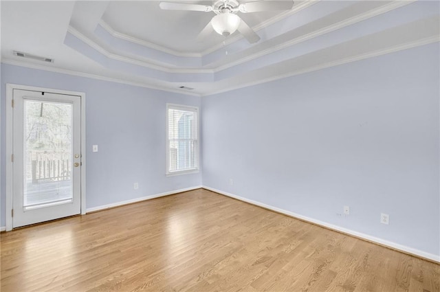 empty room featuring wood finished floors, visible vents, baseboards, ornamental molding, and a raised ceiling