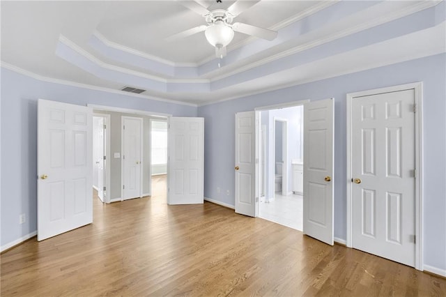 unfurnished bedroom with wood finished floors, visible vents, baseboards, ornamental molding, and a tray ceiling